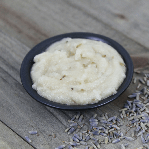 Lavender grapefruit body polish in a small black dish sitting on a wood plank
